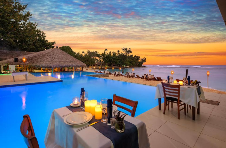 Dining setup by a pool with a sunset over the ocean. Wander Beyond Co Womens Group Trips to Vanuatu. 
